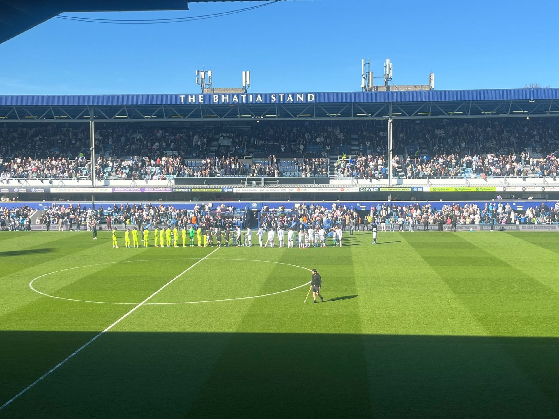 Spelers en mascottes vóór de wedstrijd op Loftus Road met The Bhatia Stand op de achtergrond